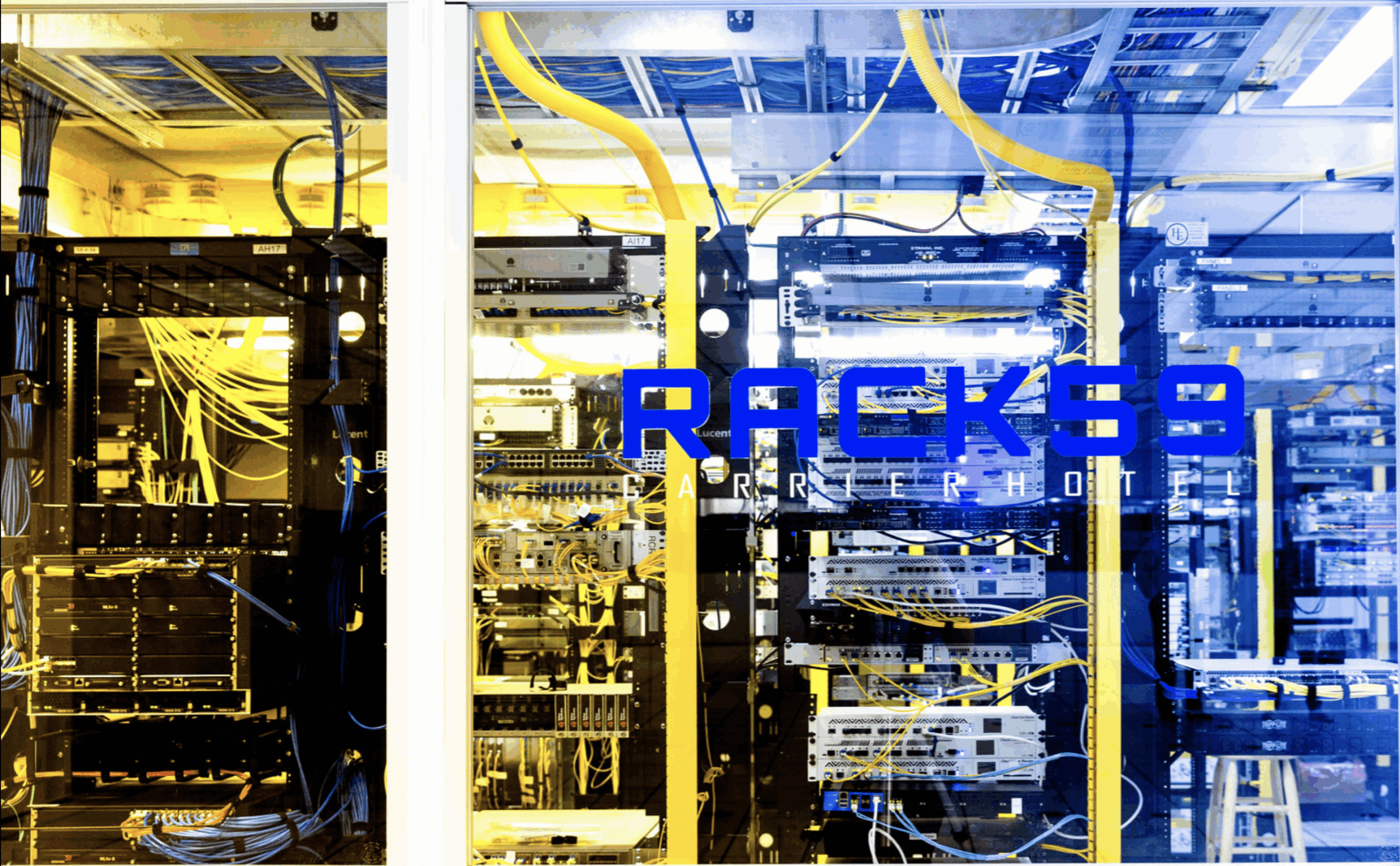 A brightly lit server room with racks of networking equipment and cables, featuring the bold blue "RACK59 CARRIER HOTEL" logo on the glass wall.